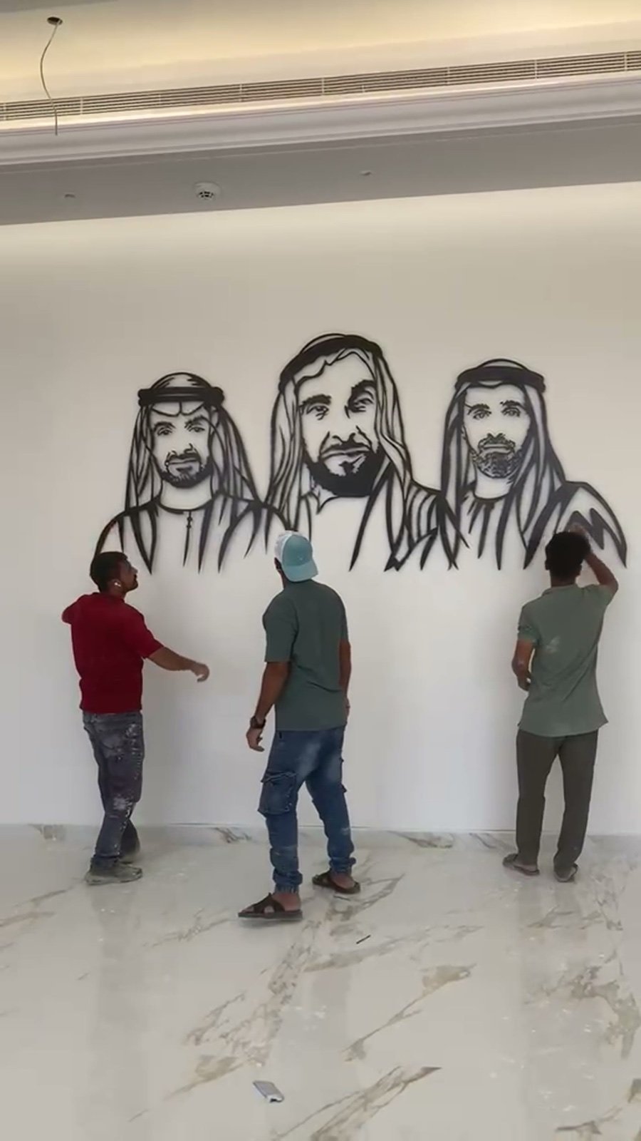 Three installers lifting a three-metre laser-cut UAE leaders metal wall art into position