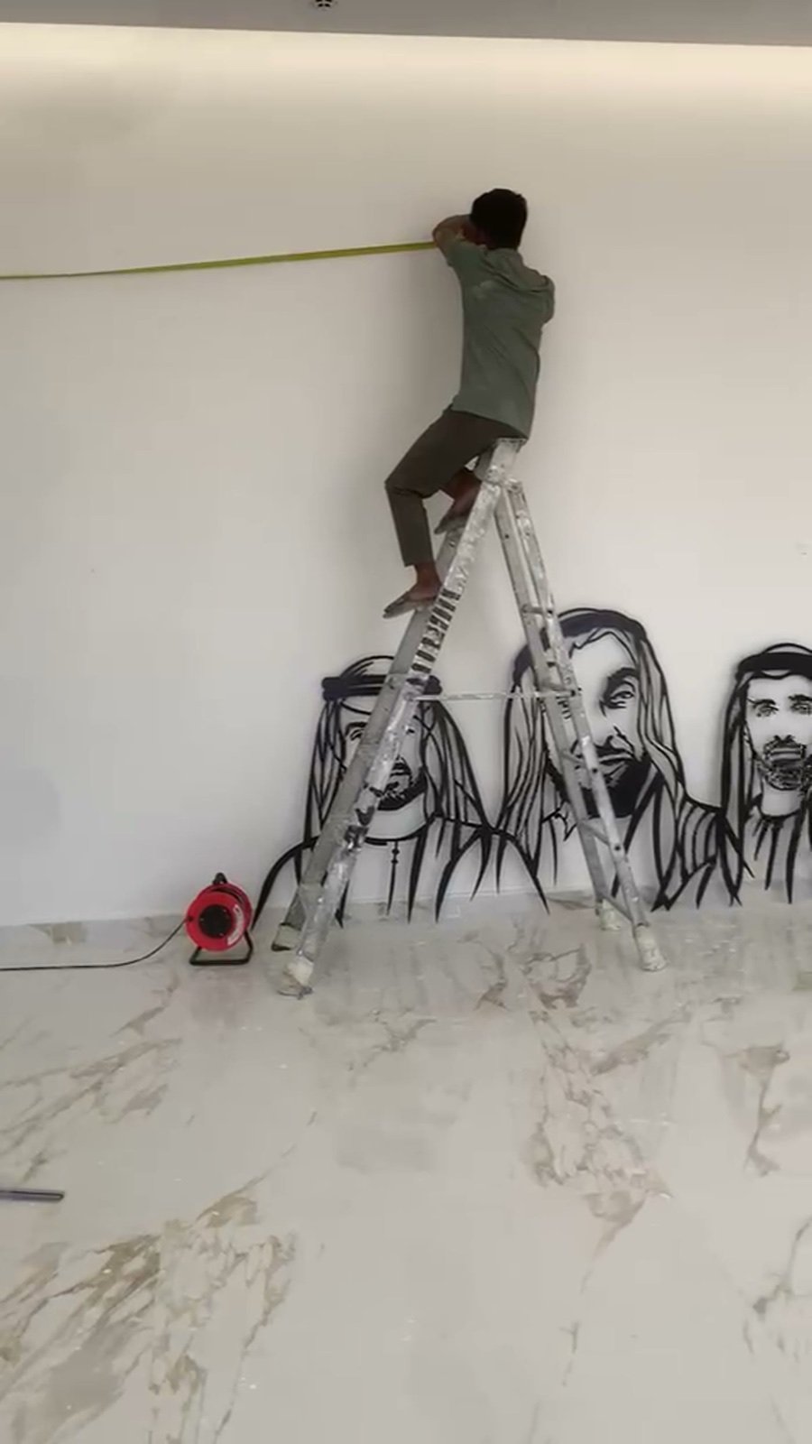 Installer on a ladder measuring and setting out levels for a large metal wall art piece