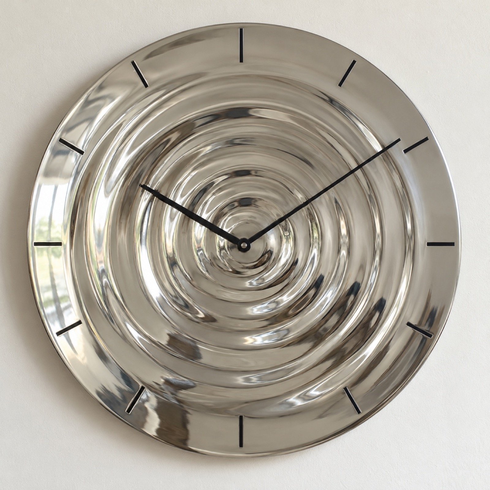 Round silver ripple wall clock with black hands on a plain white wall