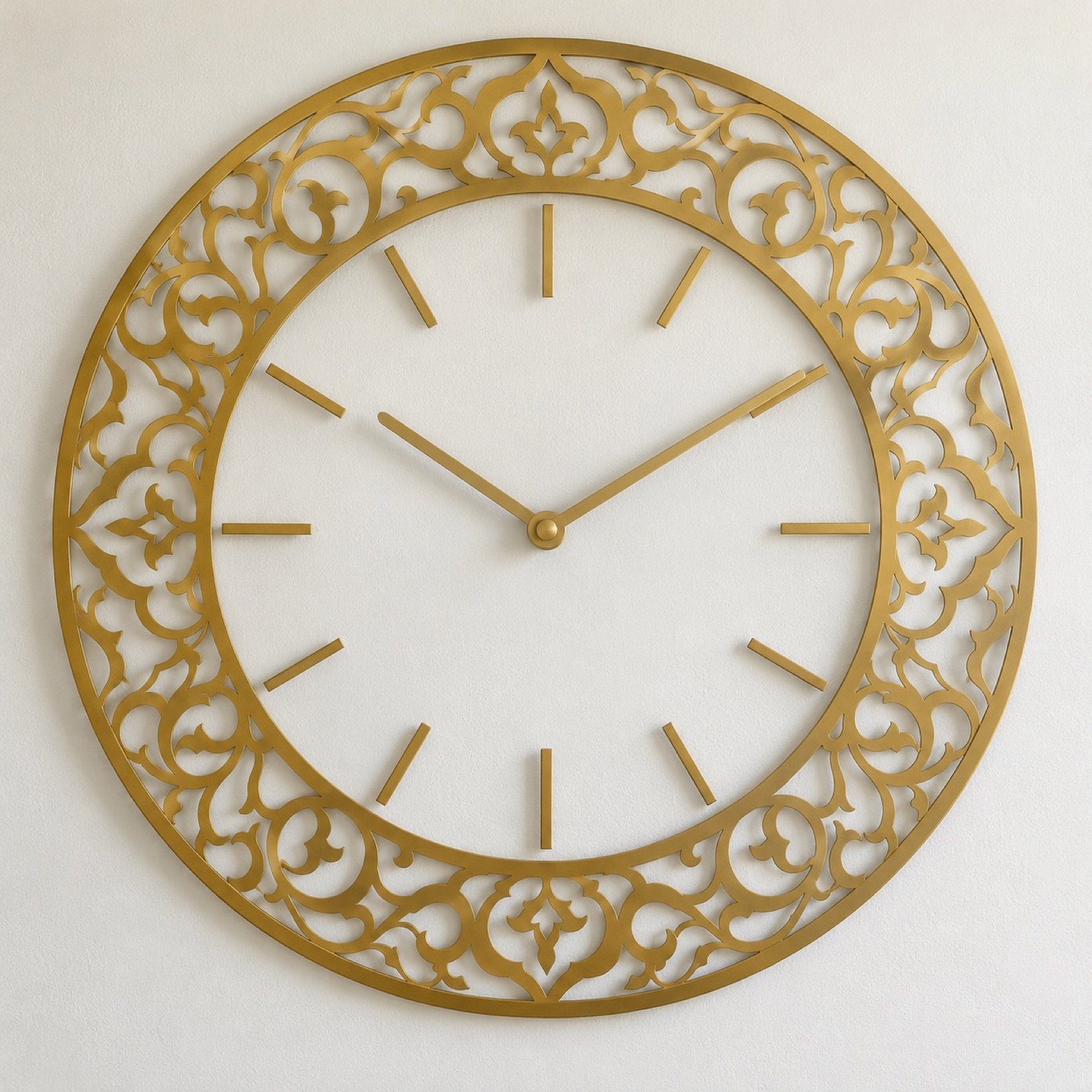 Round gold laser-cut steel wall clock with an arabesque pattern ring on a plain white wall.