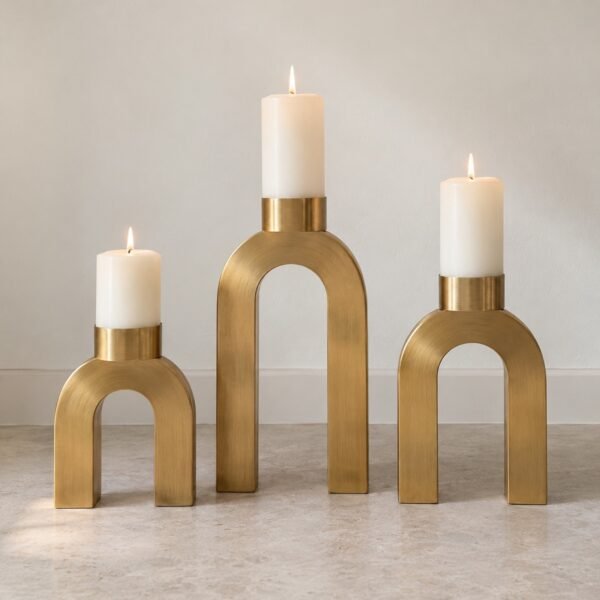 Brass arch candle holder trio with white pillar candles against a plain white wall.