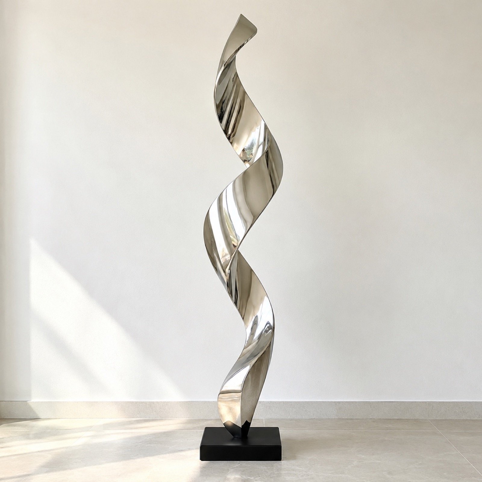 Mirror-polished stainless steel abstract wave floor sculpture on a slim black plinth against a light wall.