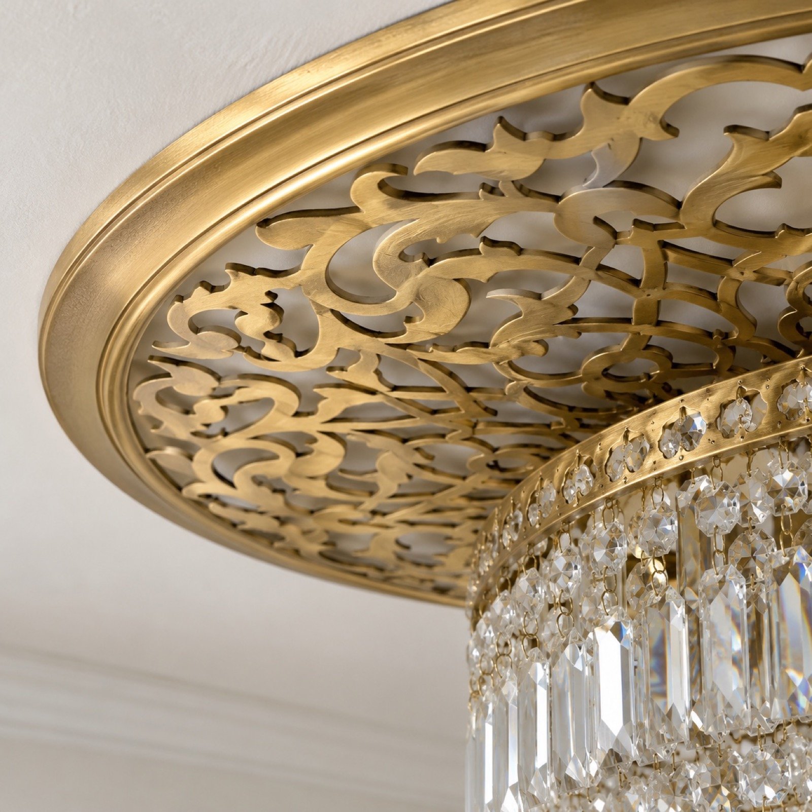 Round gold laser-cut steel ceiling medallion with crystal chandelier on a white wall