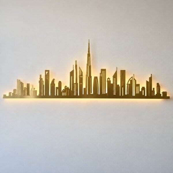 Gold PVD steel panoramic abstract skyline wall art with warm LED backlight on a plain white wall.