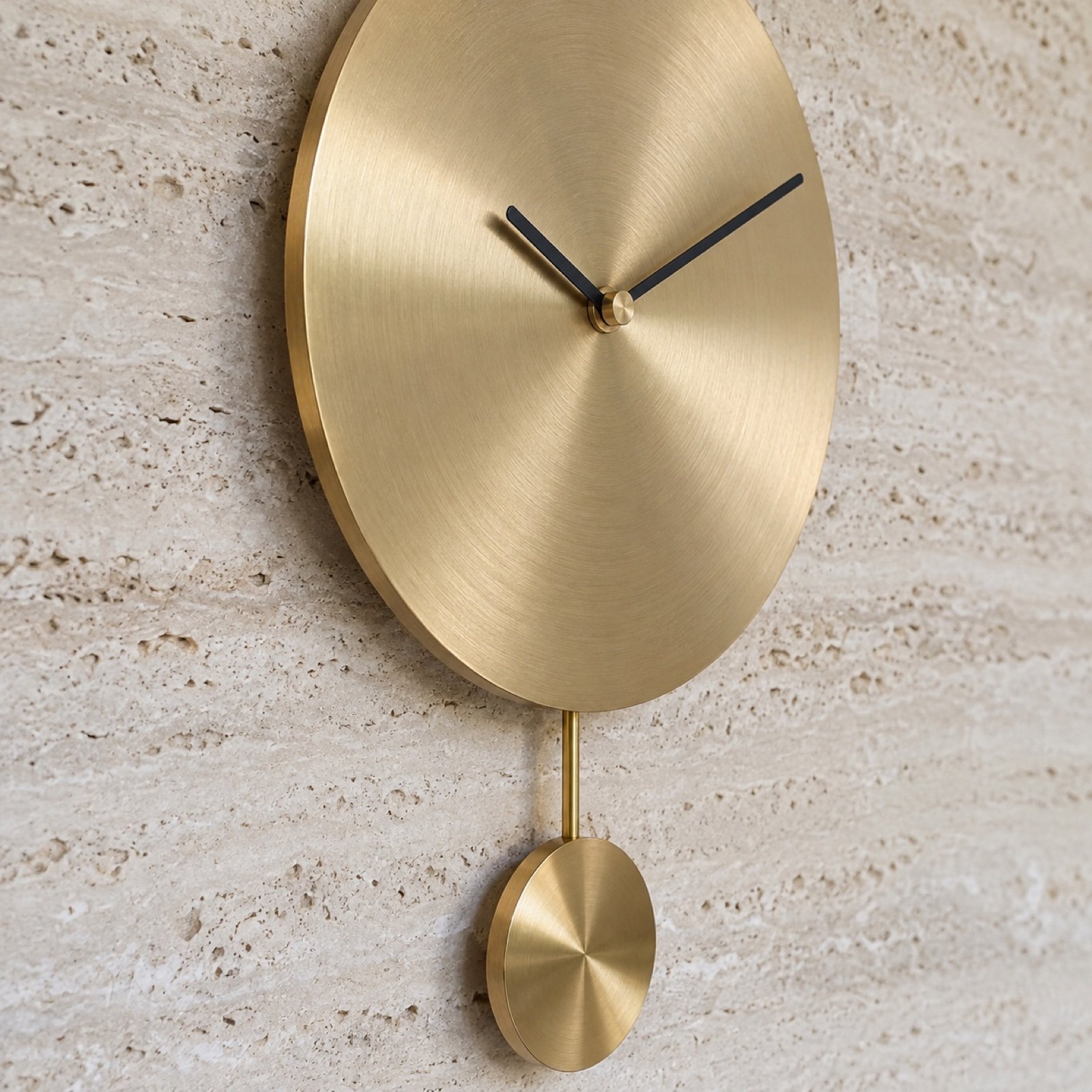 Close-up of brushed brass clock face edge, black hands, brass rod and polished pendulum disc