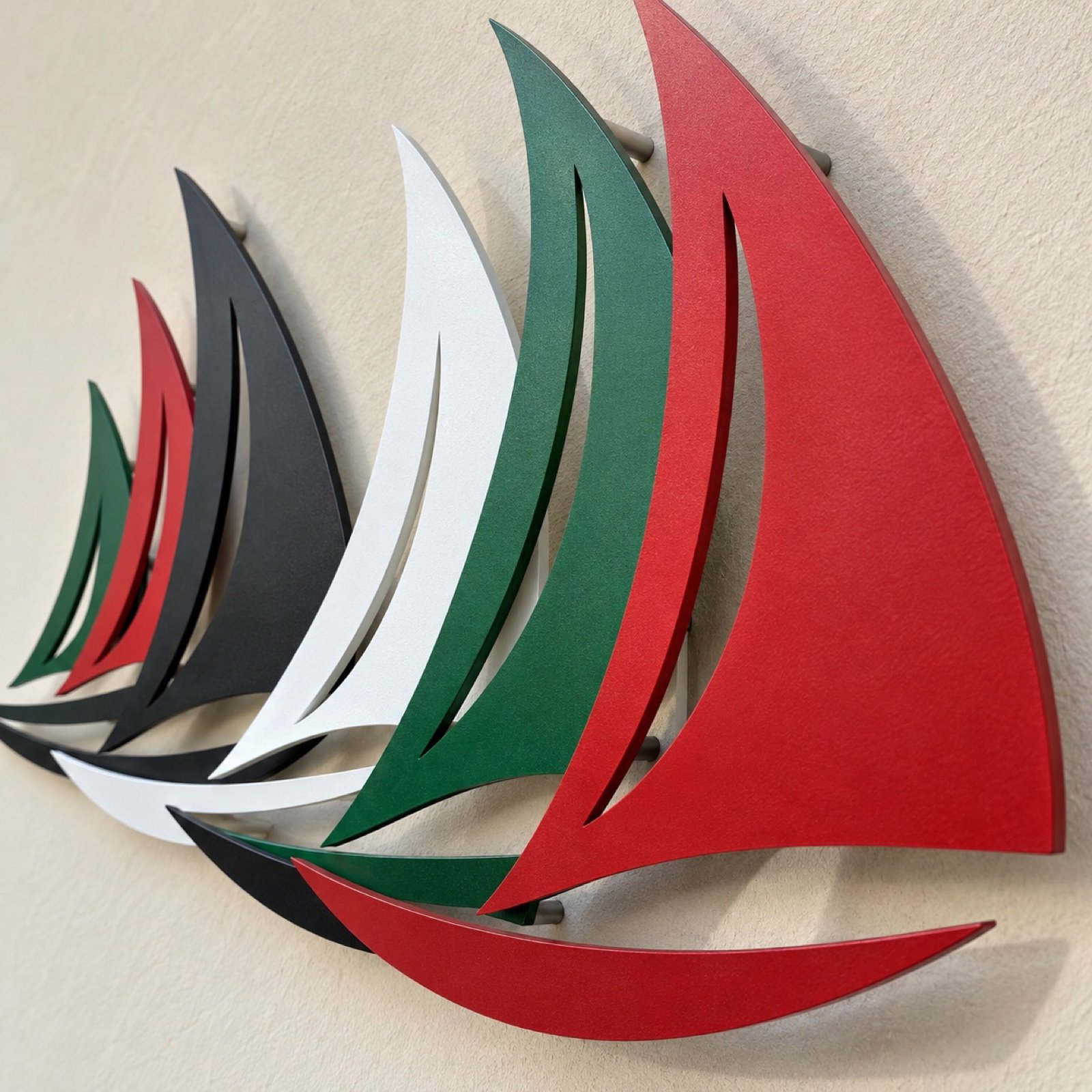 Close-up of overlapping laser-cut steel dhow sails showing powder-coated edges and metal depth.