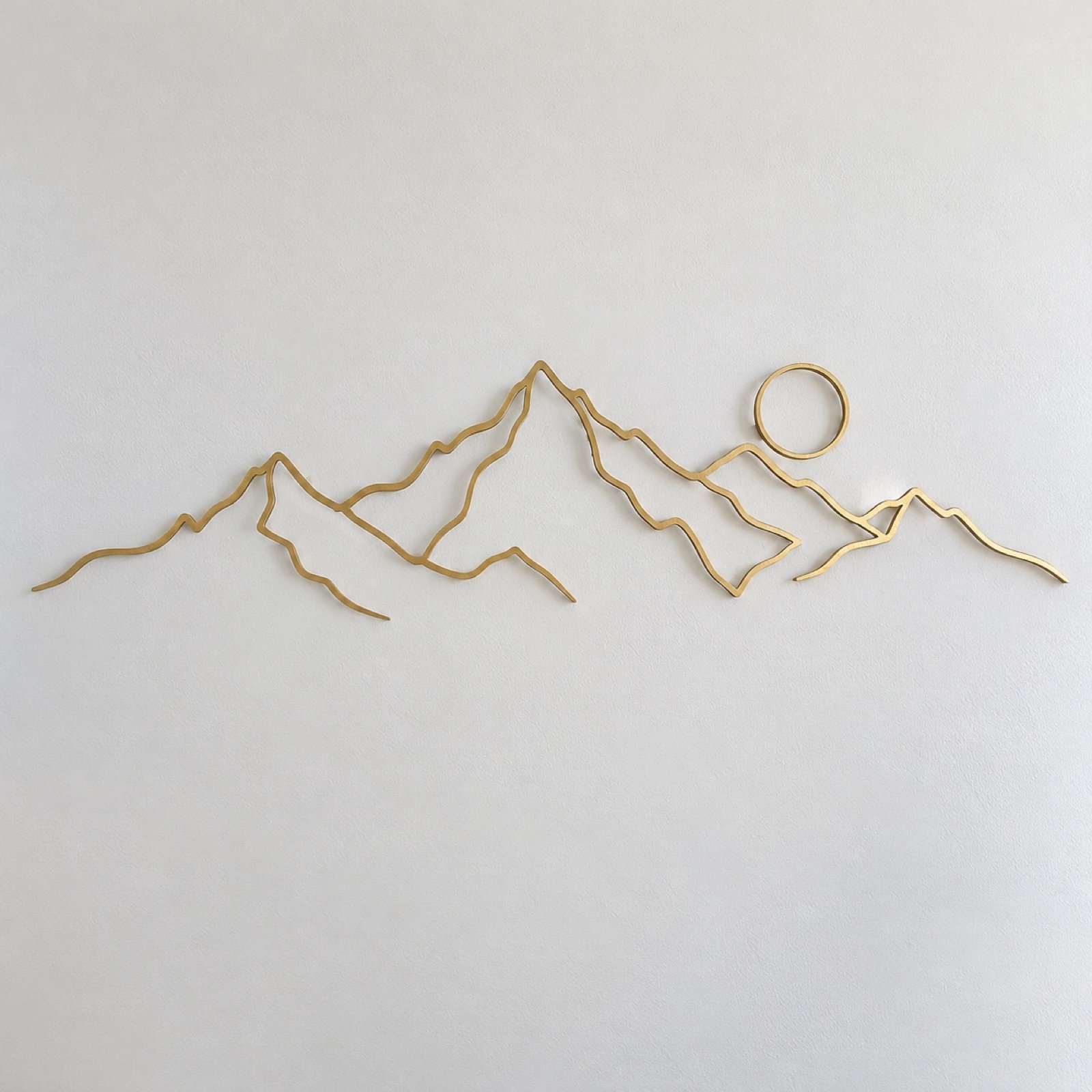 Brushed-gold minimal mountain range line art wall decor on a plain white wall.