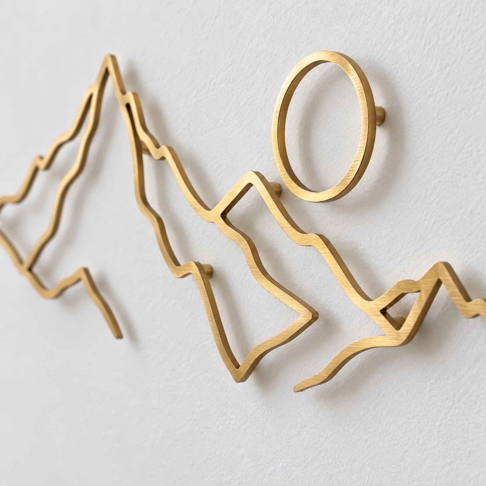Close-up of the brushed-gold metal edge and wall mounting of minimalist mountain line art.