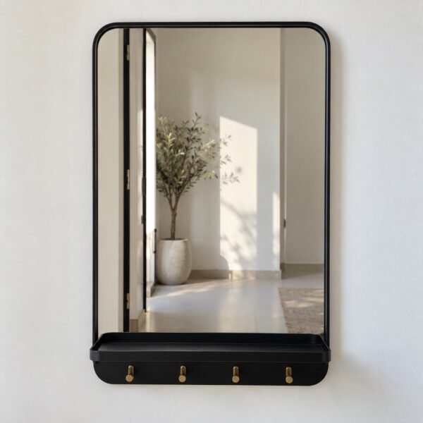 Rounded rectangular matte black entryway mirror with shelf and four brass key hooks on a plain white wall.