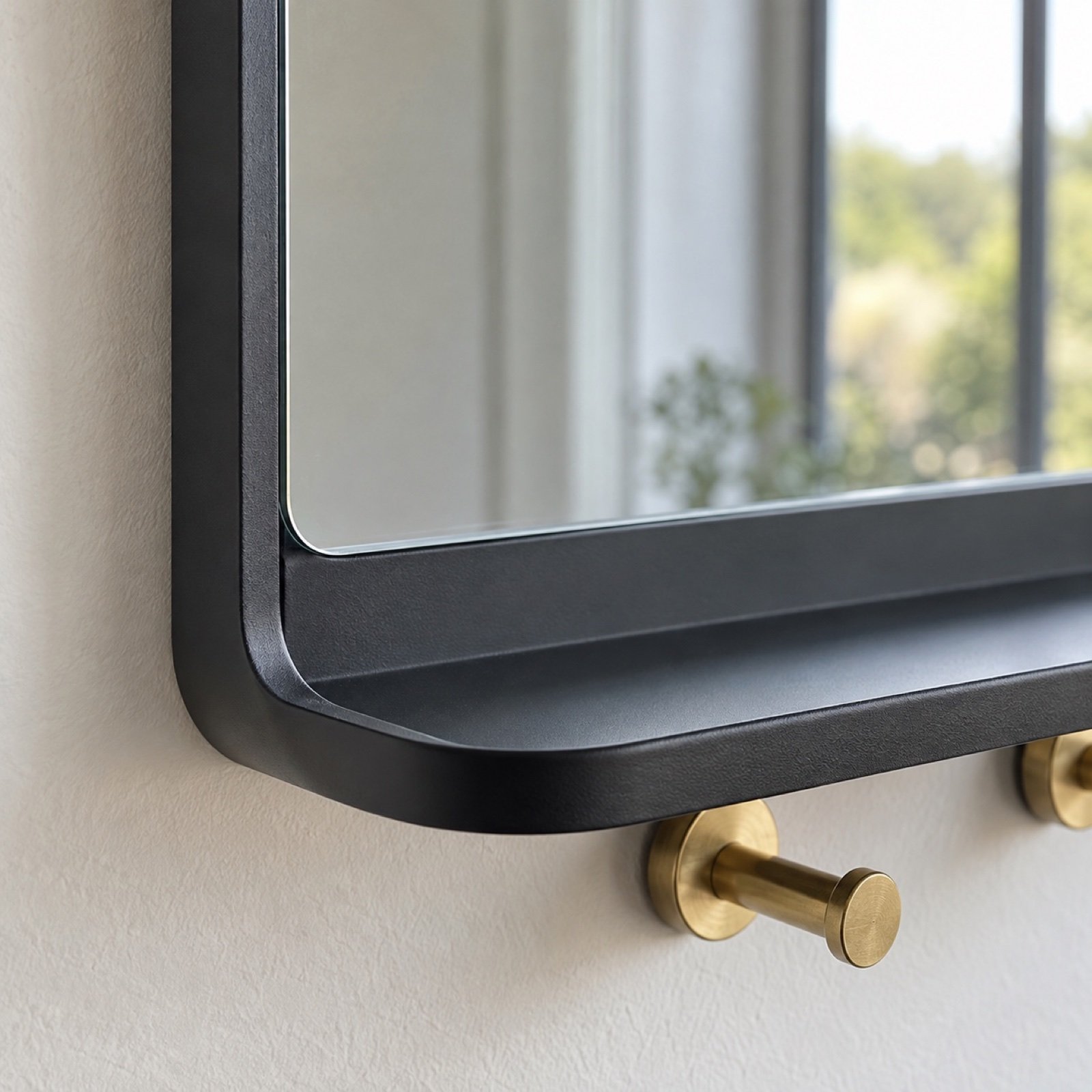 Close-up of the matte black steel frame, mirror edge, integrated shelf, and brass key hook.