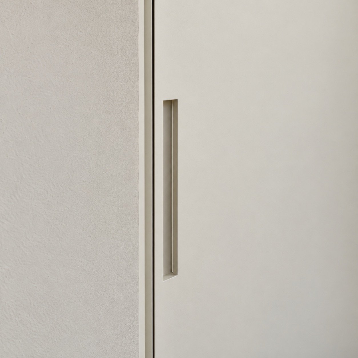 Close-up of the recessed pull and concealed frame edge on a matte off-white door
