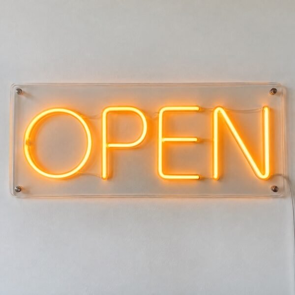 Cafe OPEN neon sign on clear acrylic against a white wall, front view.