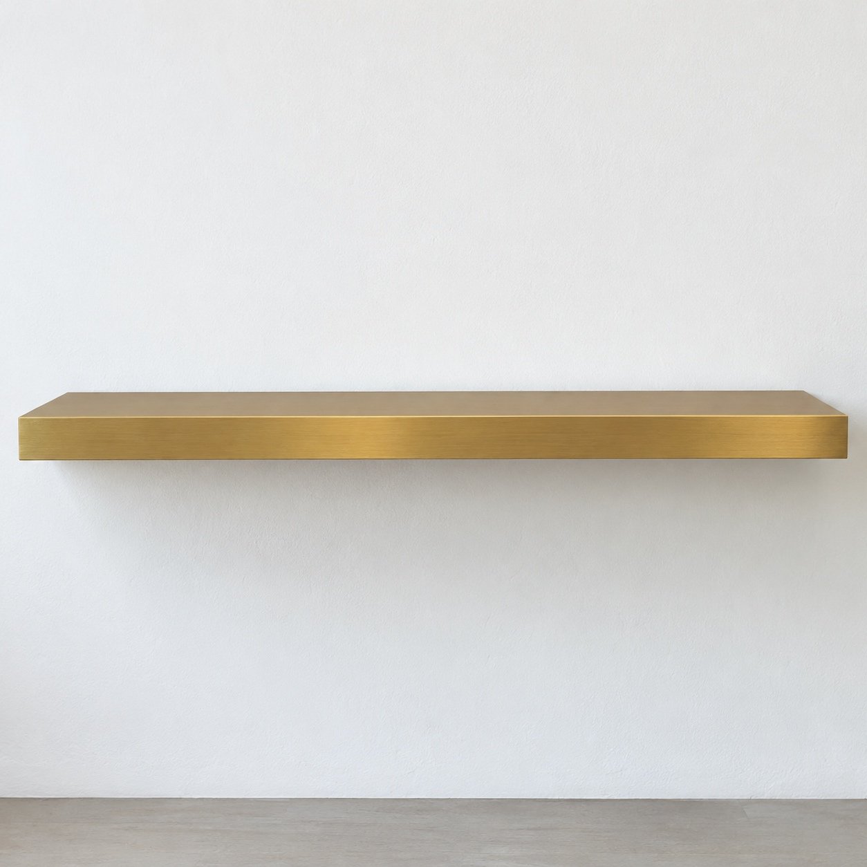 brushed gold steel floating wall shelf on a plain white wall, front view