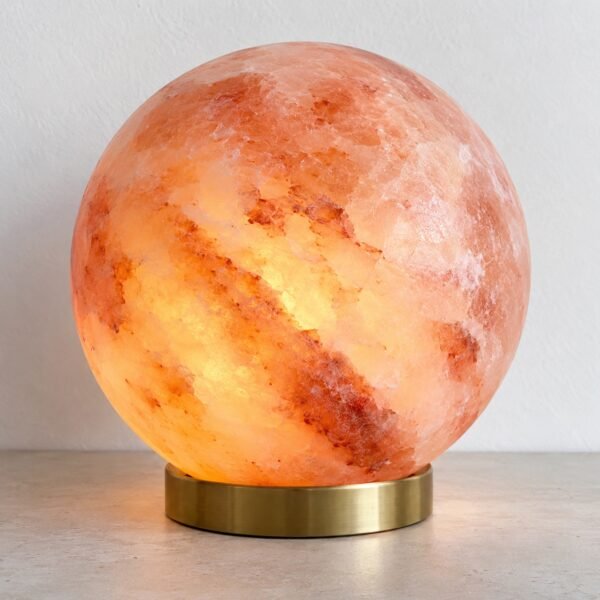 Polished natural Himalayan pink salt sphere lamp on a slim brushed-brass base against a plain white wall