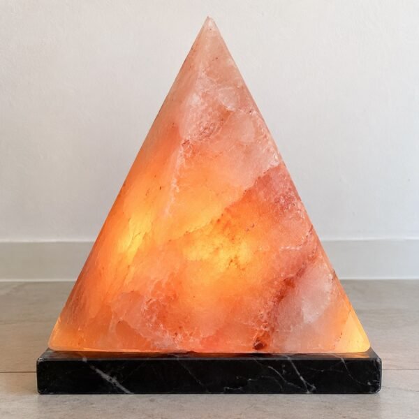 Polished pink Himalayan salt pyramid lamp on a black marble base against a white wall