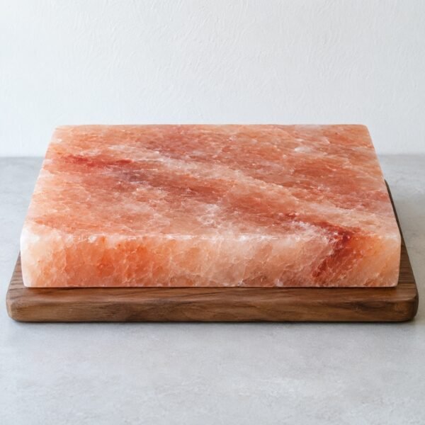 Polished rectangular Himalayan pink salt slab on a walnut serving board against a white wall