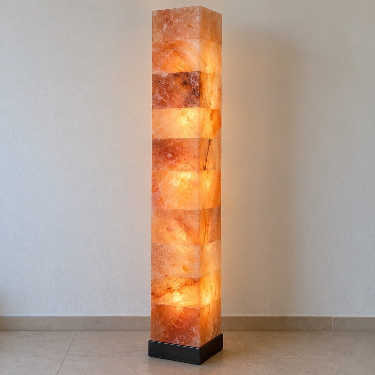 Tall square pink Himalayan salt floor column lamp on a black metal plinth against a plain light wall.