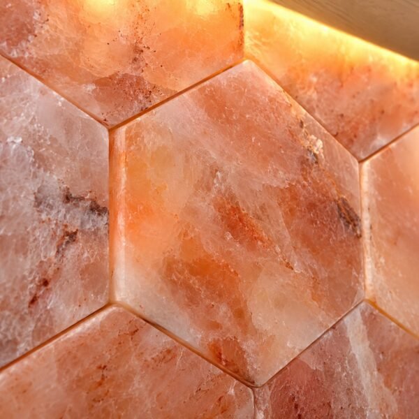 Straight-on view of smooth hexagonal Himalayan pink salt wall tiles on a plain white wall.