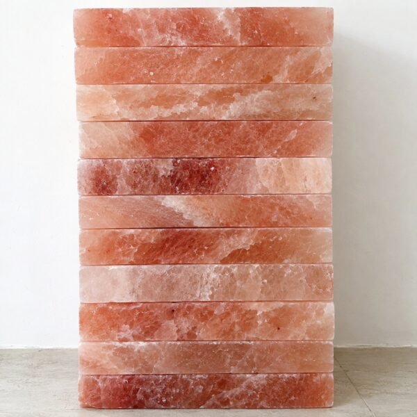Stack of natural Himalayan pink salt bricks on a light floor against a white wall