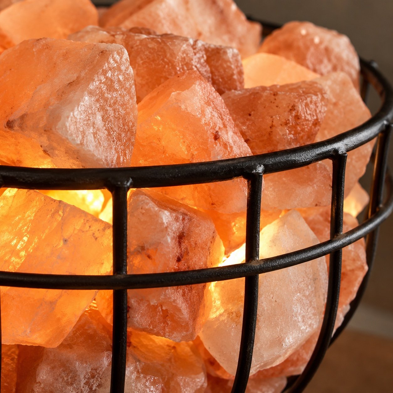 Close-up of rough pink Himalayan salt chunks and black iron wire basket edge with warm glow