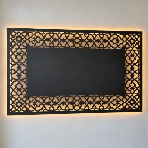 Front view of a charcoal powder-coated steel TV wall panel with an arabesque laser-cut border and warm LED backlight on a white wall.