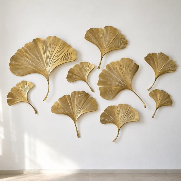 Nine brushed gold PVD steel ginkgo leaves scattered on a white wall.