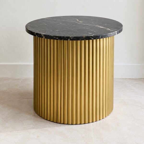 Round fluted gold steel side table with a black marble top on a light floor