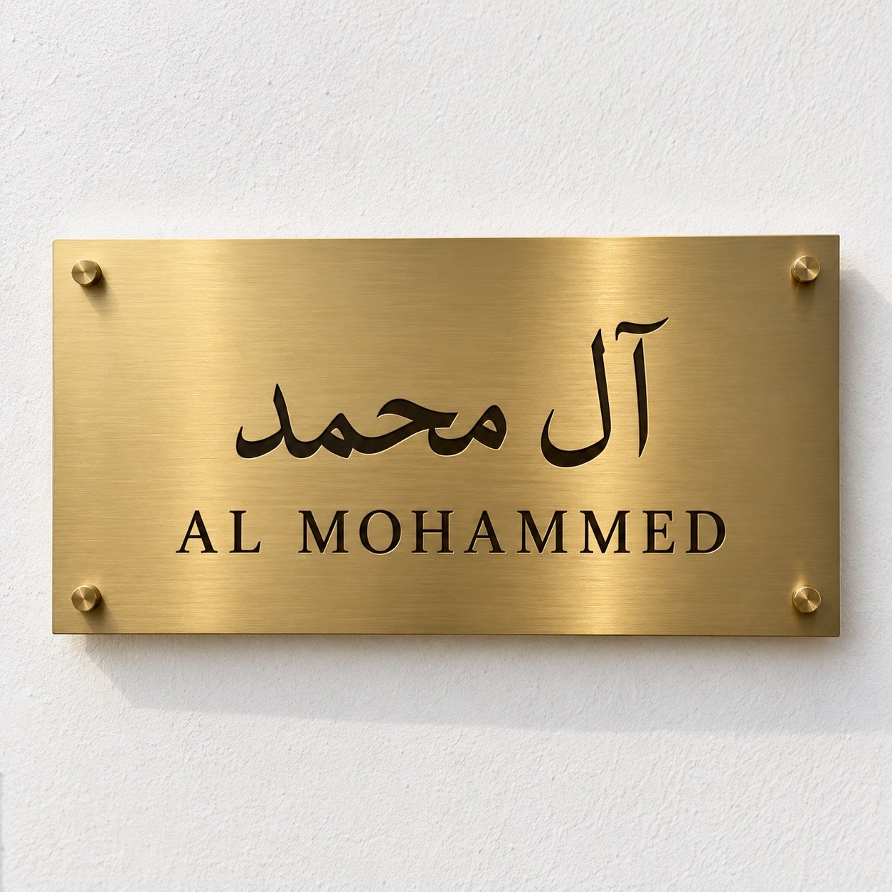 Gold PVD stainless steel villa name plate with Arabic آل محمد and English AL MOHAMMED on a white wall.