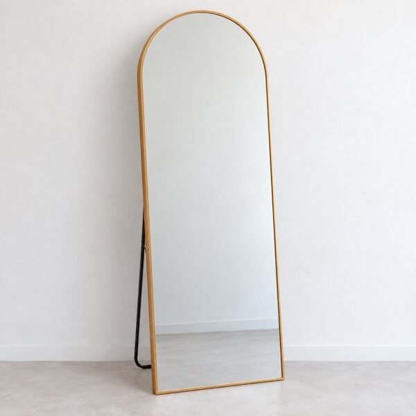 Arched warm-gold metal floor mirror standing against a plain white wall