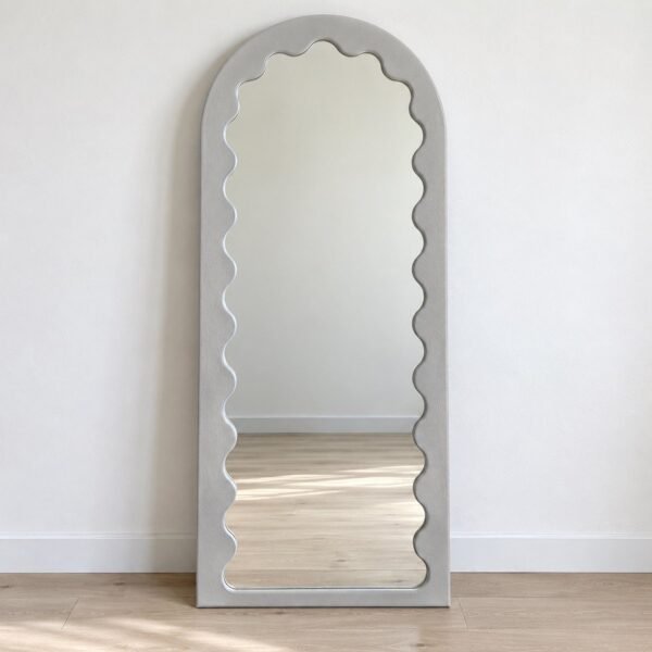 Full-length light grey arched floor mirror with a scalloped inner edge against a plain white wall.