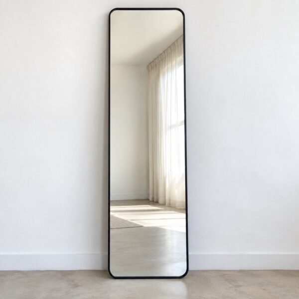 Noorline charcoal-black framed leaner mirror standing against a plain white wall on a pale floor.