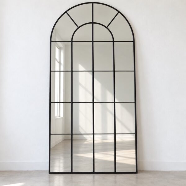 Arched black grid leaner mirror standing against a plain white wall