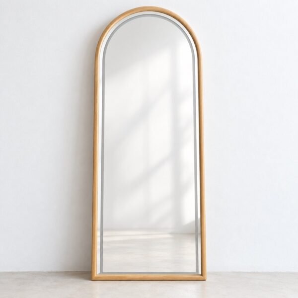 Full-length arched leaner mirror with a warm light natural-wood frame against a plain white wall.