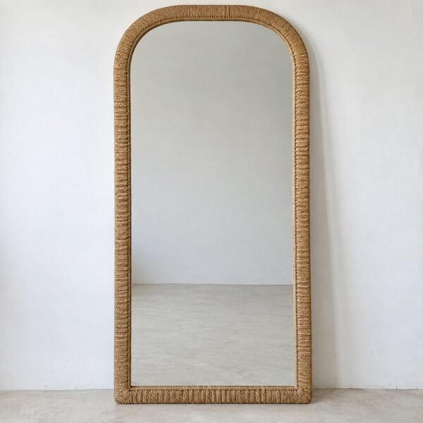 Full-length woven rattan arch leaner mirror against a plain white wall