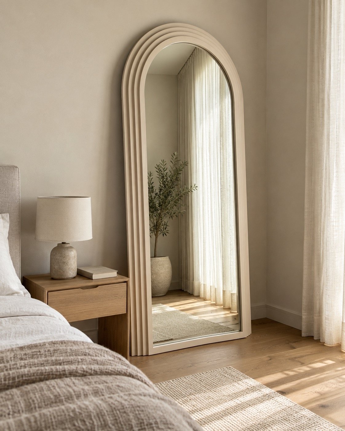 Warm ivory arched leaner mirror beside a bedside table in a bedroom corner