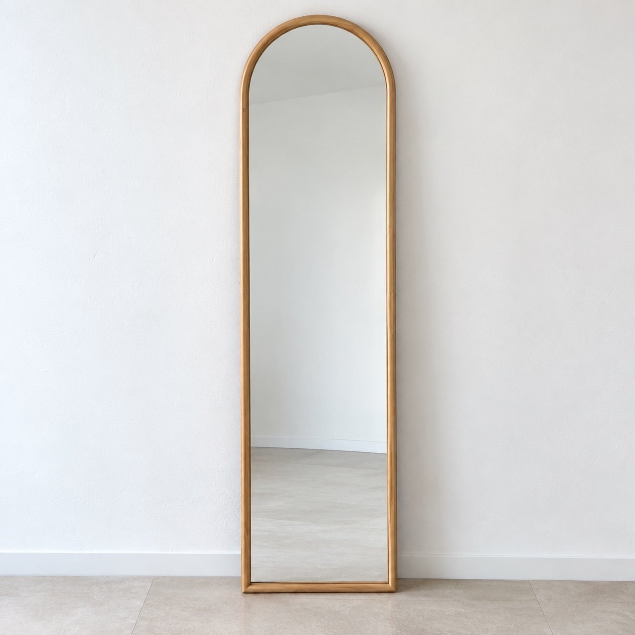 Layan light warm natural-wood capsule leaner mirror standing against a plain white wall