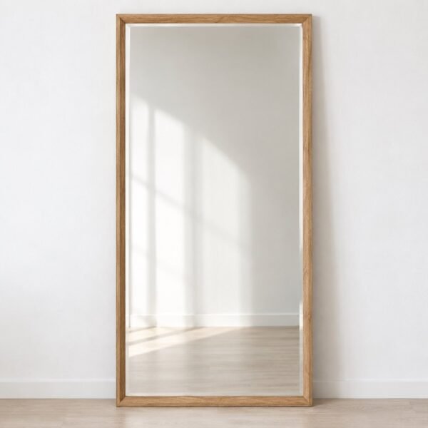 Full-length rectangular light-oak leaner mirror standing against a plain white wall.