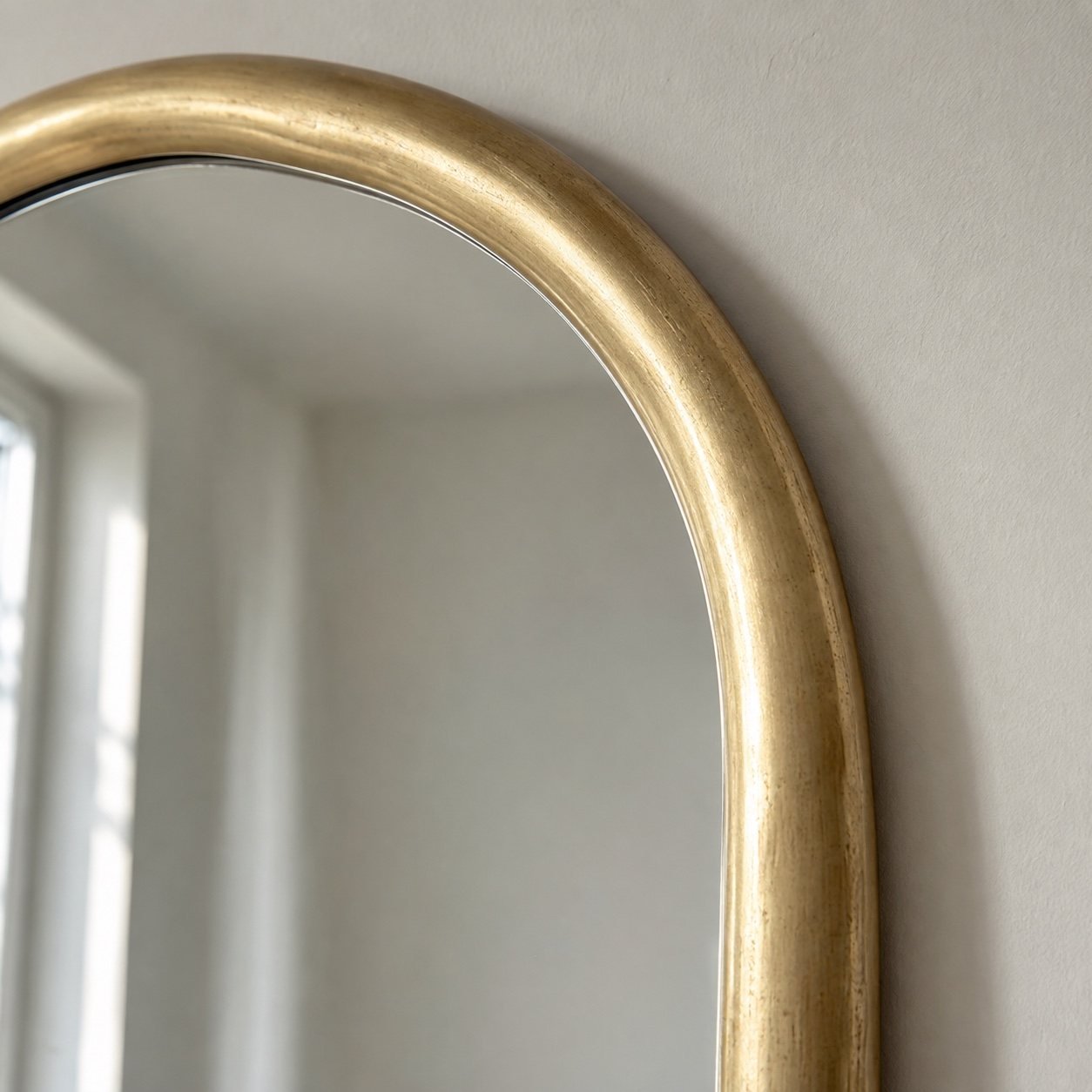 Close-up of the warm champagne-gold metal frame and clean mirror edge on the Sahra organic mirror.
