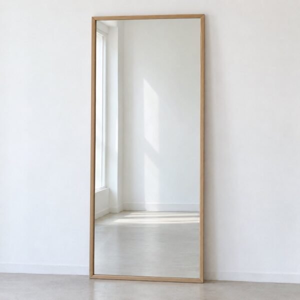 Full-length rectangular leaner mirror with a slim warm light-oak wood frame against a white wall.