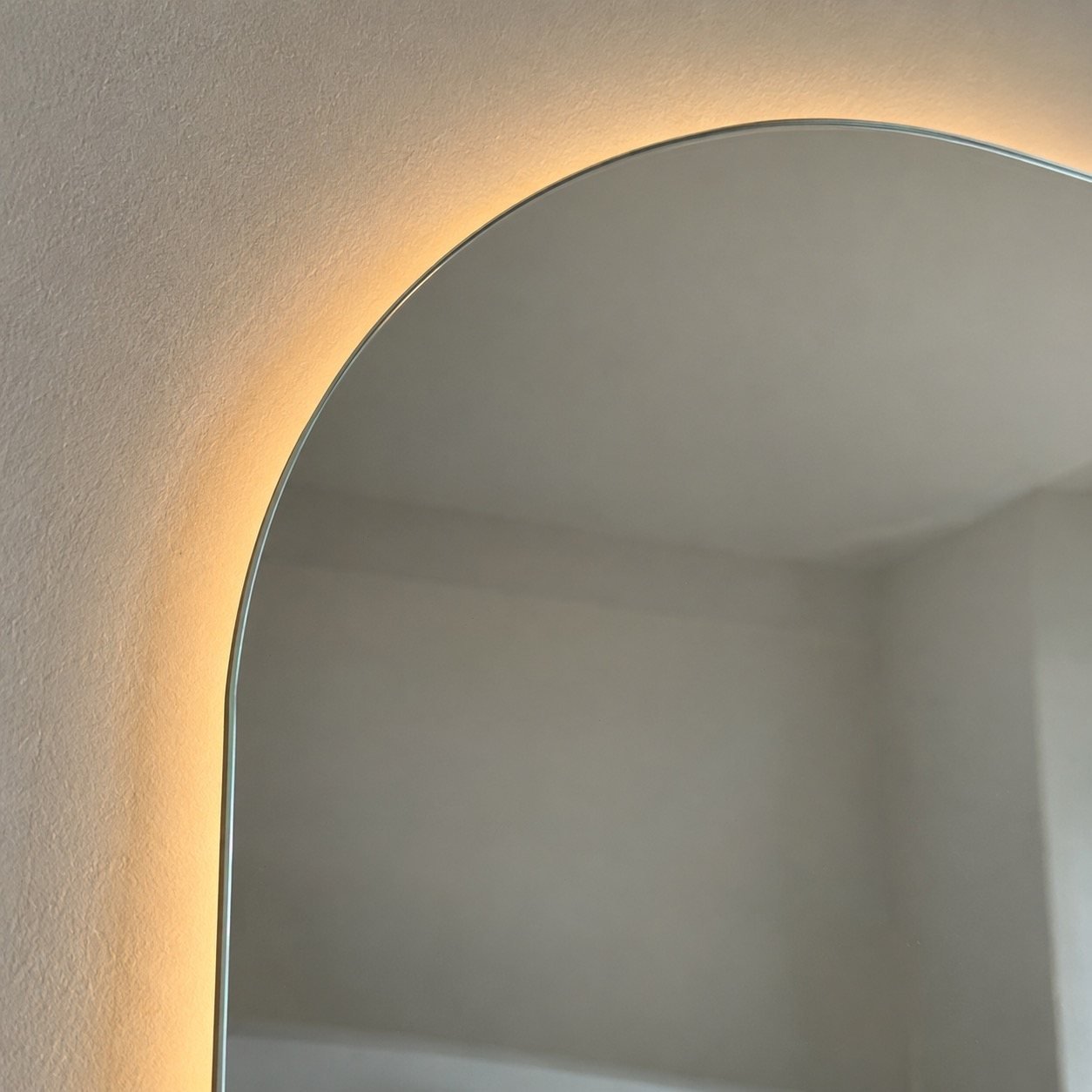 Close-up of the curved glass edge and warm LED halo on Nour Arc mirror