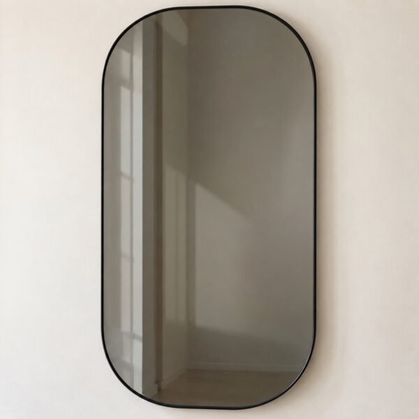 Smoked grey capsule mirror with slim matte black frame on a plain white wall, front view.
