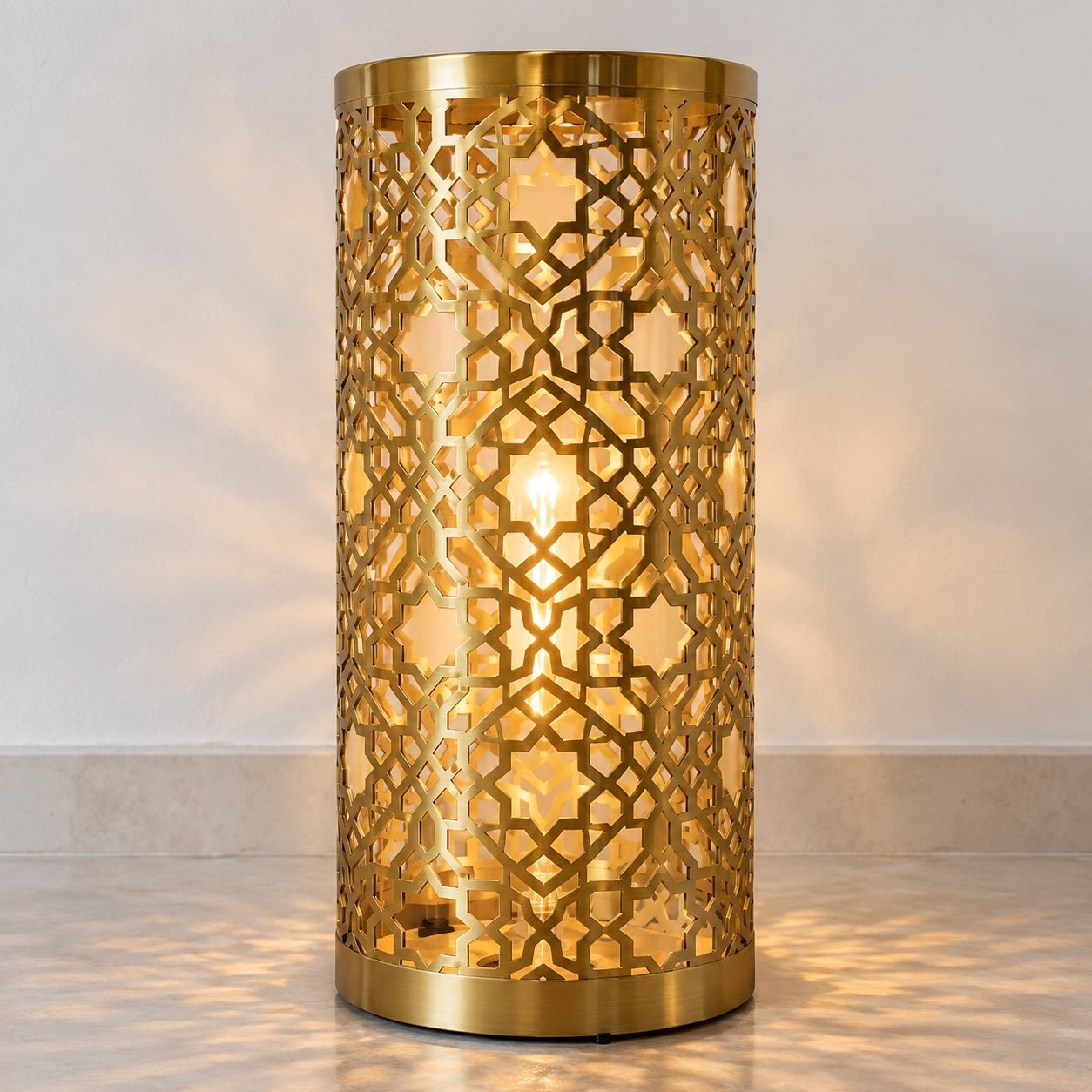 Cylindrical gold PVD steel Islamic pattern table lantern on a plain white wall.
