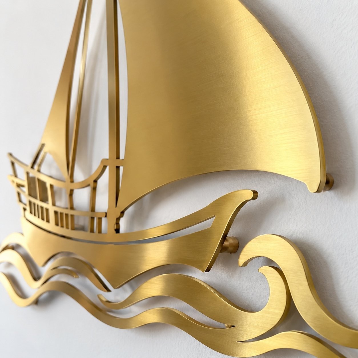 Close-up of the gold PVD steel dhow wall art showing the curved sail, cut edge and wall shadow