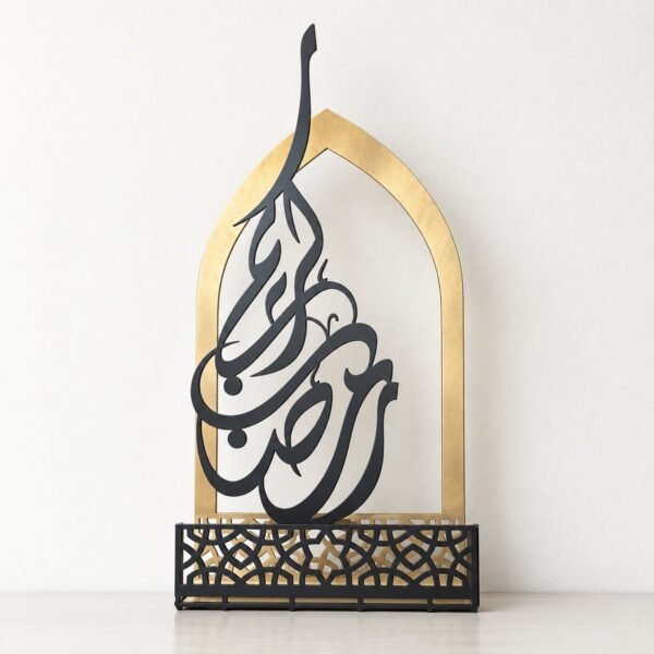 Front view of a gold and dark charcoal Ramadan Kareem metal tabletop decoration against a warm-white wall.