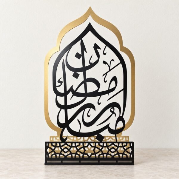 Ramadan Mubarak gold and black tabletop metal decoration shown front-facing against a warm-white wall.